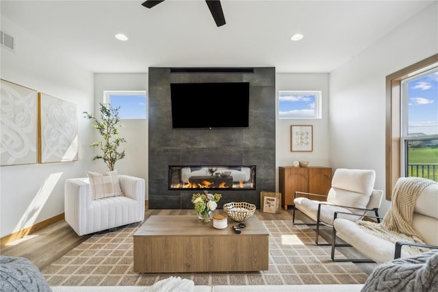 living room with ceiling fan, light hardwood / wood-style floors, and a tiled fireplace