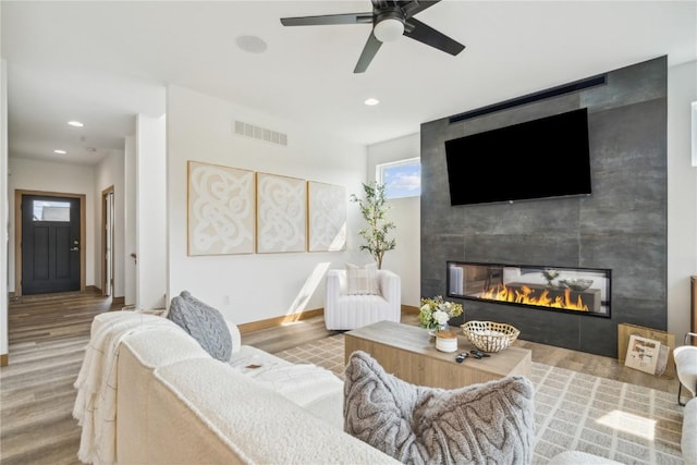 living room featuring a tile fireplace, ceiling fan, and wood-type flooring