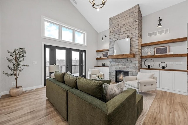 living room with a high ceiling, french doors, a fireplace, light hardwood / wood-style floors, and a chandelier