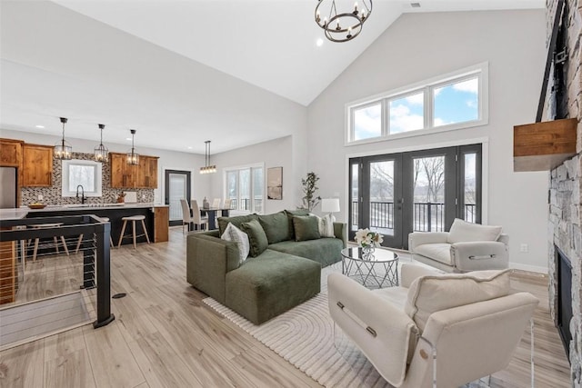 living room featuring high vaulted ceiling, french doors, sink, a fireplace, and a chandelier