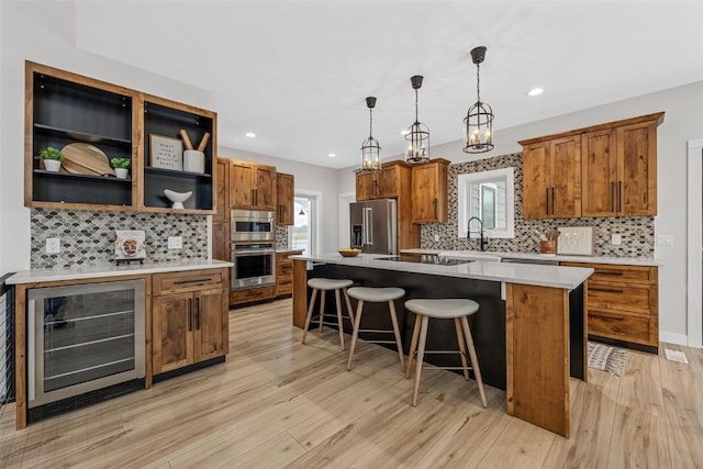 kitchen featuring appliances with stainless steel finishes, beverage cooler, decorative light fixtures, light hardwood / wood-style floors, and a kitchen island