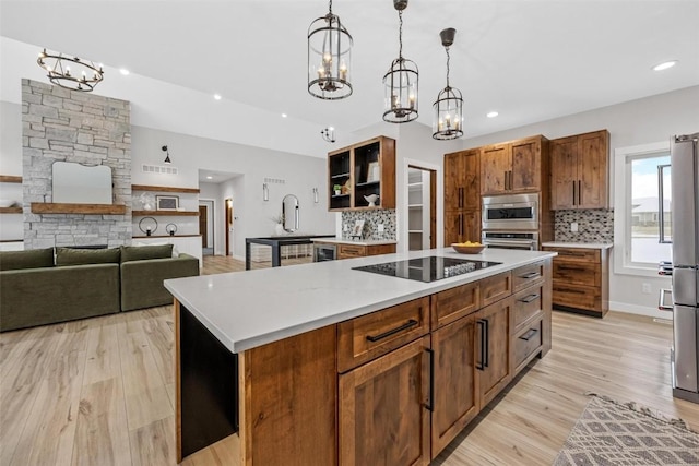 kitchen with light wood-type flooring, backsplash, stainless steel appliances, decorative light fixtures, and a kitchen island