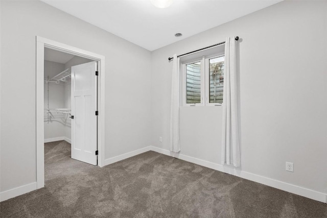 unfurnished bedroom with a spacious closet, a closet, and dark carpet