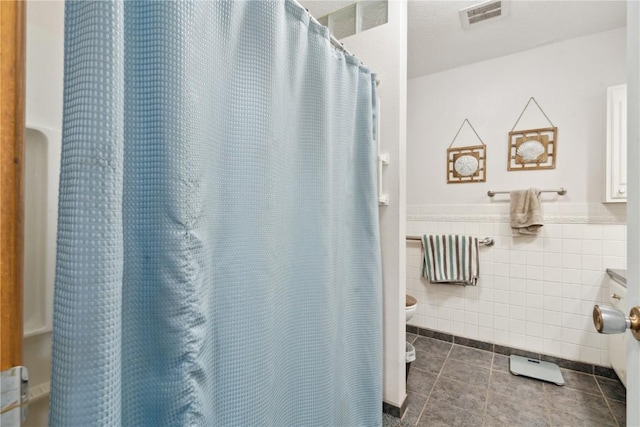 bathroom with toilet, tile patterned floors, and tile walls