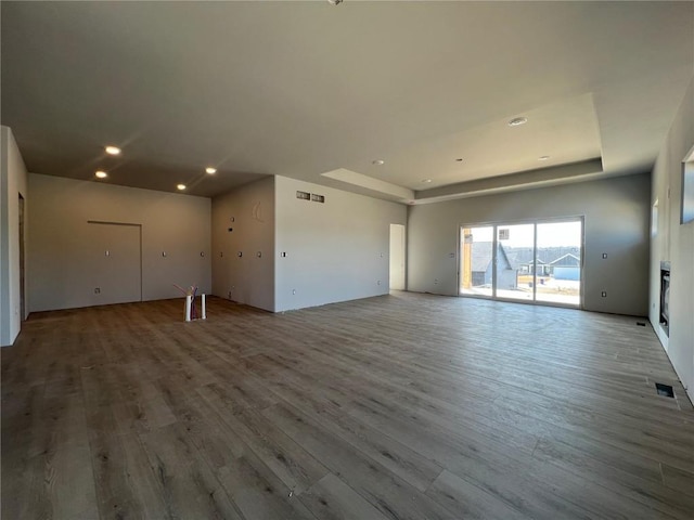 unfurnished living room with a raised ceiling, recessed lighting, wood finished floors, and visible vents