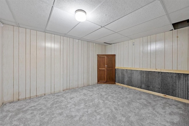 basement with a paneled ceiling, carpet floors, and wooden walls