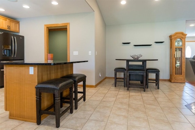 kitchen with a kitchen bar, black refrigerator with ice dispenser, and light tile patterned flooring