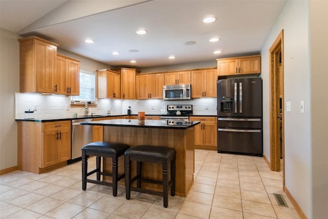 kitchen with vaulted ceiling, light tile patterned floors, appliances with stainless steel finishes, a kitchen island, and a kitchen bar