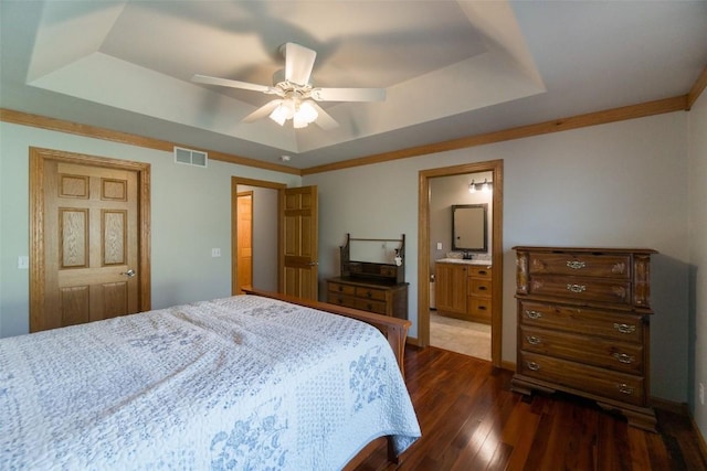 bedroom with ceiling fan, dark hardwood / wood-style floors, a raised ceiling, and connected bathroom