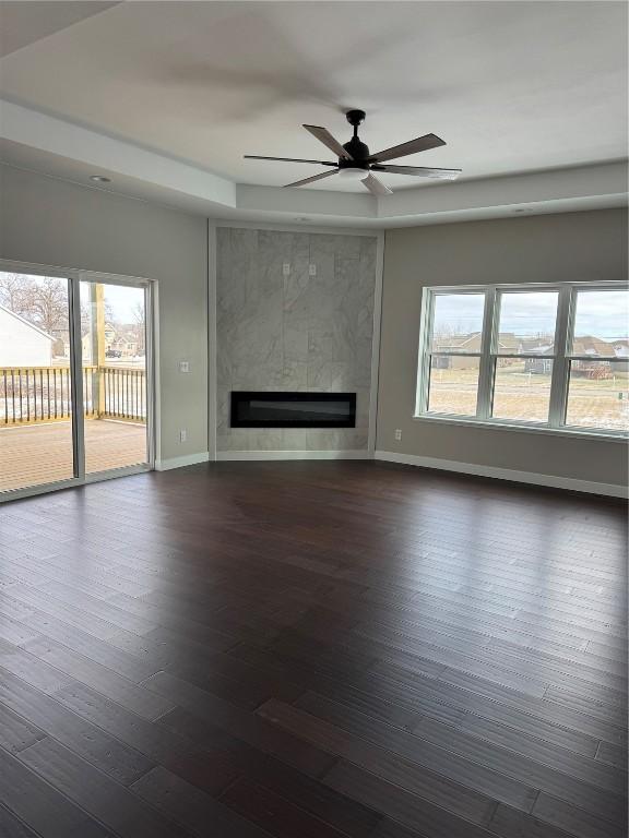 unfurnished living room featuring ceiling fan, dark hardwood / wood-style floors, a raised ceiling, and a tile fireplace