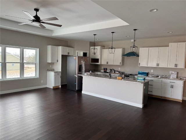 kitchen with light stone countertops, a kitchen island with sink, white cabinets, and hanging light fixtures