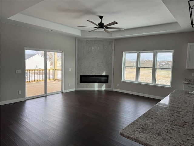 unfurnished living room featuring a large fireplace, a raised ceiling, and dark wood-type flooring