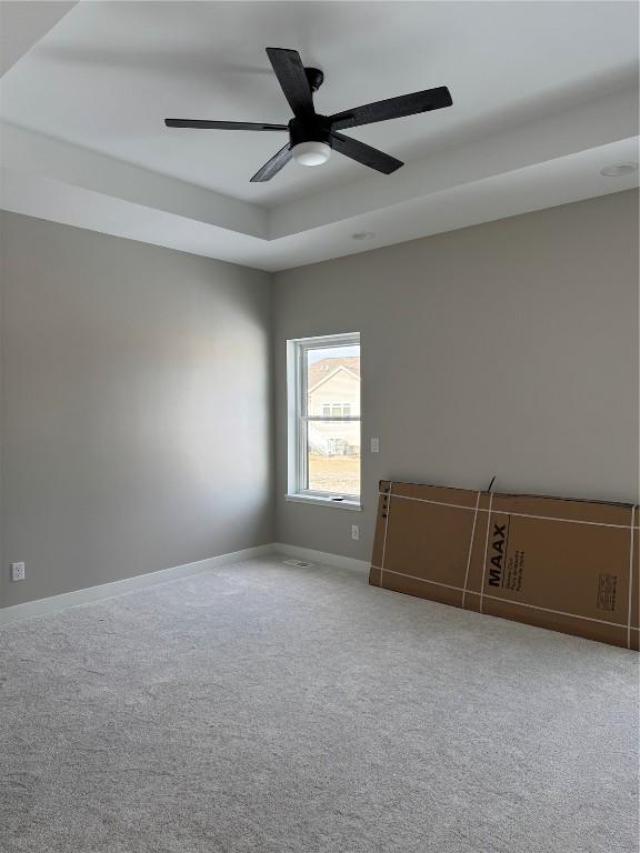 spare room featuring a tray ceiling, ceiling fan, and carpet