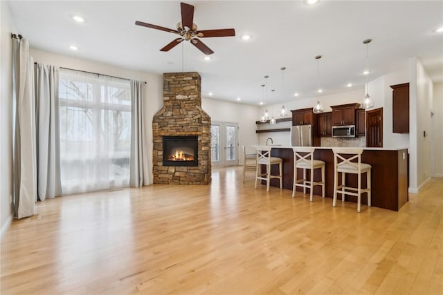 living area featuring ceiling fan, a stone fireplace, light wood-style flooring, and recessed lighting