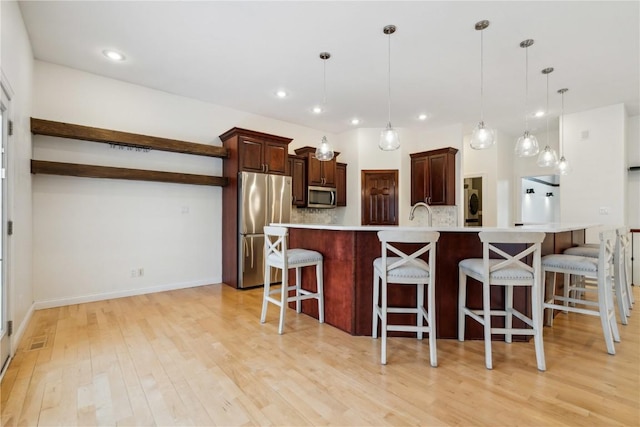 kitchen featuring light wood-style flooring, stainless steel appliances, a kitchen breakfast bar, light countertops, and tasteful backsplash