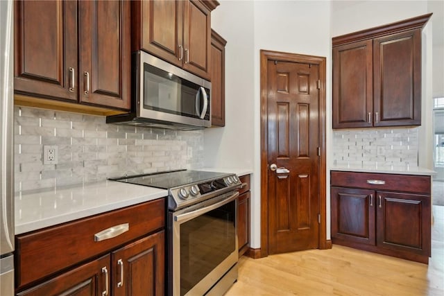 kitchen with light wood finished floors, appliances with stainless steel finishes, light countertops, and decorative backsplash