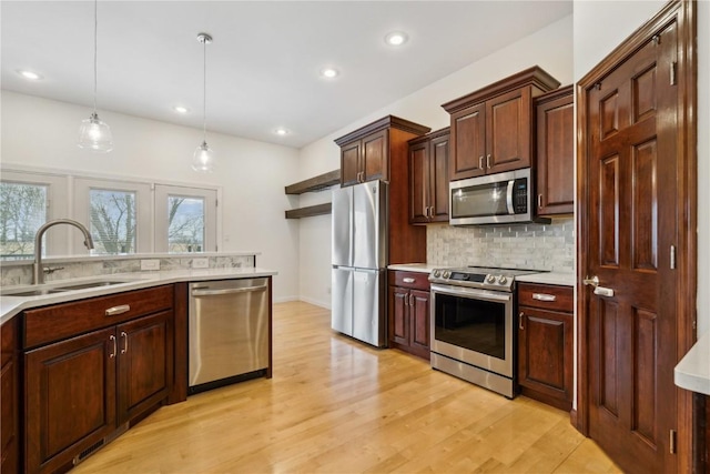 kitchen featuring appliances with stainless steel finishes, hanging light fixtures, light countertops, light wood-style floors, and a sink