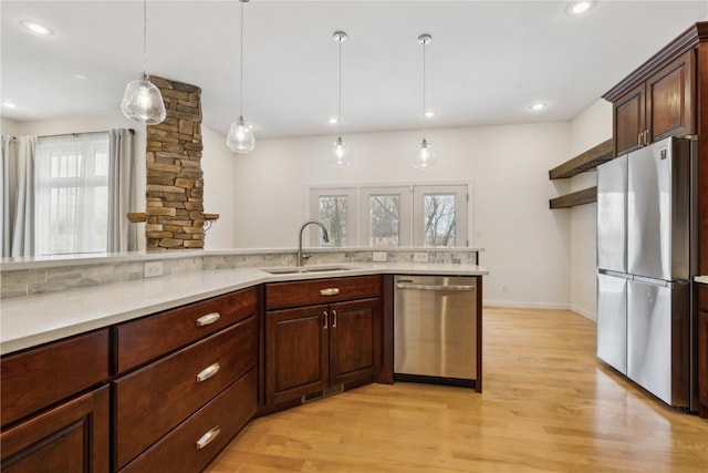 kitchen featuring light wood-style flooring, stainless steel appliances, a sink, light countertops, and decorative light fixtures