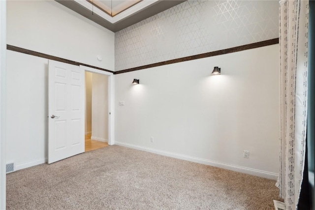 carpeted empty room with a high ceiling, visible vents, and baseboards