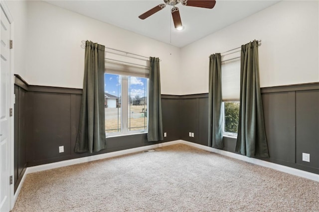 spare room featuring wainscoting, carpet flooring, and ceiling fan