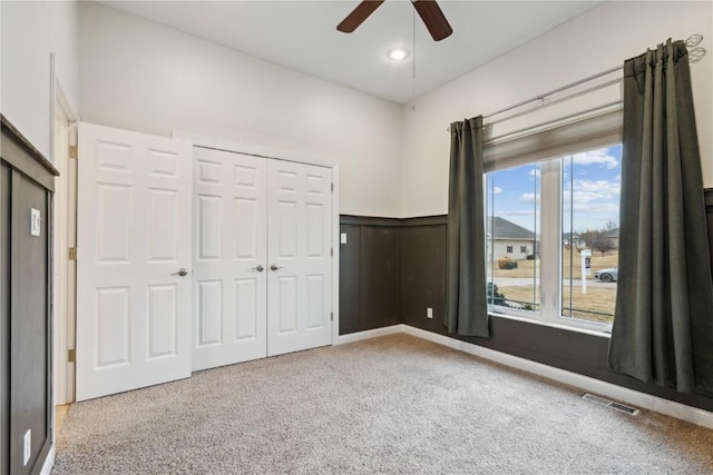 unfurnished bedroom featuring visible vents, a ceiling fan, a closet, wainscoting, and carpet