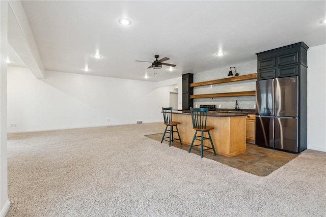 kitchen with dark countertops, a breakfast bar, freestanding refrigerator, carpet, and open shelves