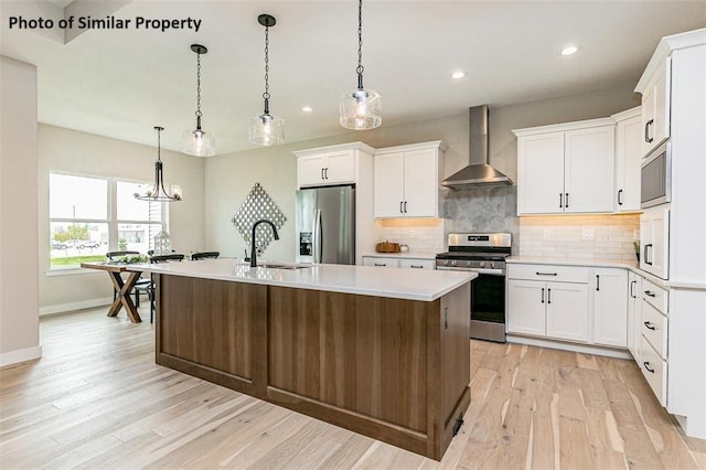 kitchen featuring pendant lighting, white cabinets, sink, wall chimney exhaust hood, and stainless steel appliances