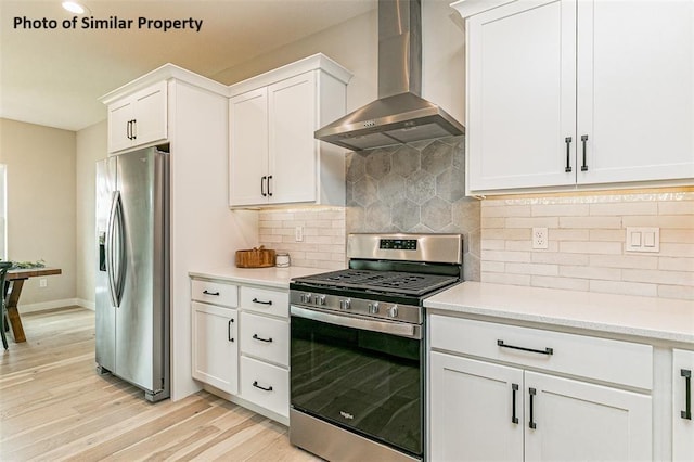 kitchen with appliances with stainless steel finishes, backsplash, wall chimney exhaust hood, light hardwood / wood-style flooring, and white cabinetry