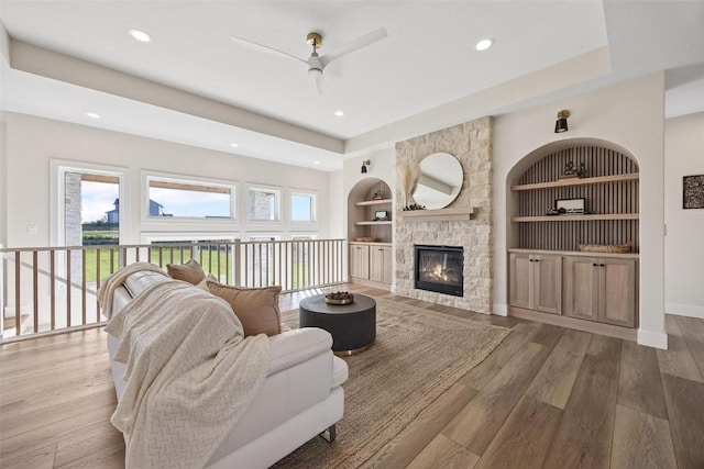 living room with built in shelves, ceiling fan, a stone fireplace, and hardwood / wood-style flooring