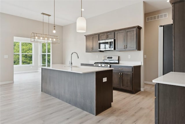 kitchen featuring appliances with stainless steel finishes, a kitchen island with sink, sink, light hardwood / wood-style flooring, and hanging light fixtures