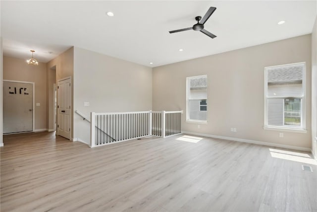 unfurnished room featuring ceiling fan with notable chandelier and light wood-type flooring