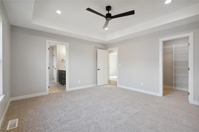 unfurnished bedroom with ensuite bath, ceiling fan, a spacious closet, a tray ceiling, and a closet