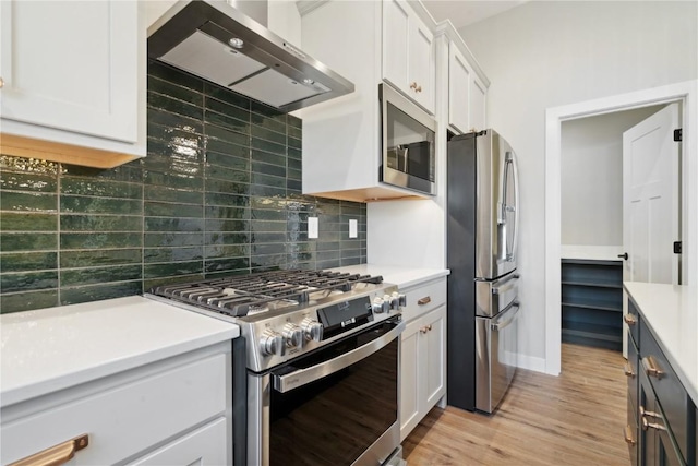 kitchen featuring white cabinets, light hardwood / wood-style flooring, wall chimney exhaust hood, appliances with stainless steel finishes, and tasteful backsplash