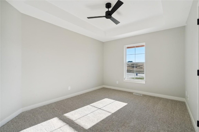 empty room with ceiling fan, carpet floors, and a tray ceiling