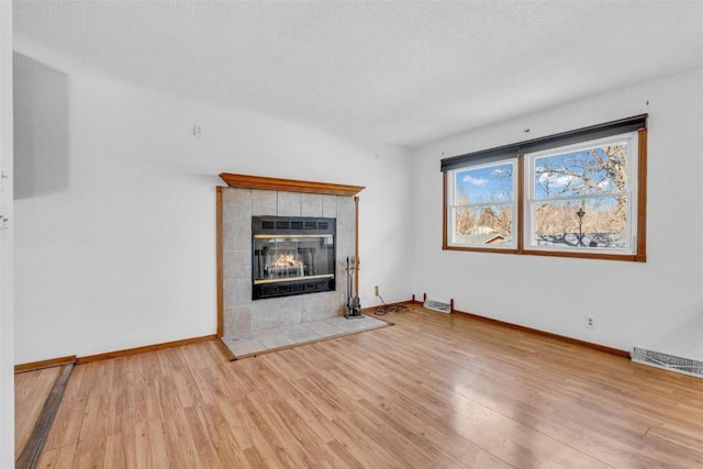 unfurnished living room featuring a textured ceiling, wood finished floors, visible vents, baseboards, and a tiled fireplace