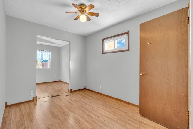 spare room featuring ceiling fan, light wood finished floors, a textured ceiling, and baseboards