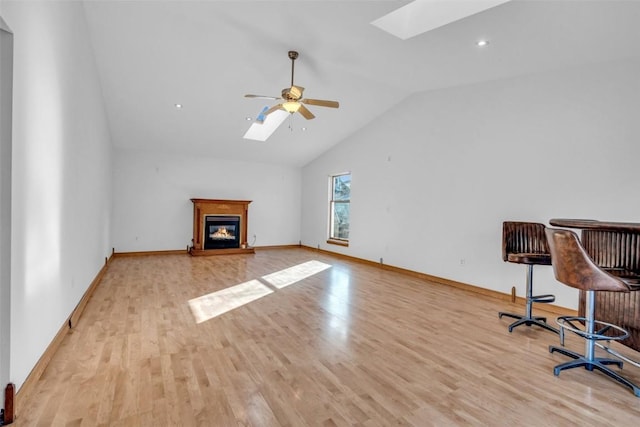 unfurnished living room with ceiling fan, vaulted ceiling with skylight, wood finished floors, and a glass covered fireplace