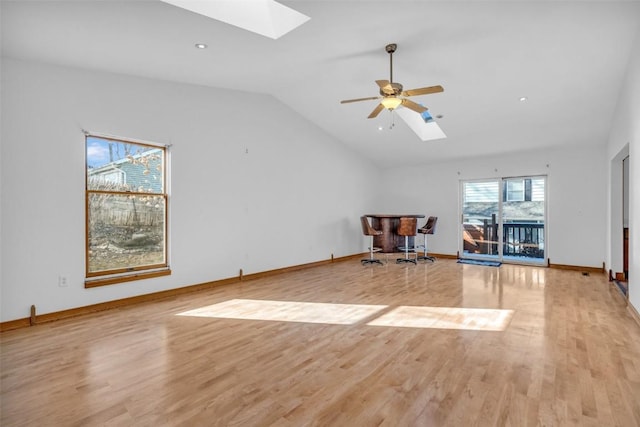 interior space with a ceiling fan, vaulted ceiling with skylight, baseboards, and light wood finished floors