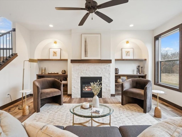 living room with hardwood / wood-style floors, ceiling fan, and a stone fireplace