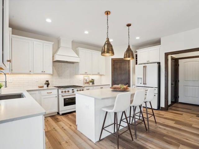 kitchen with custom exhaust hood, white appliances, white cabinets, sink, and a kitchen island