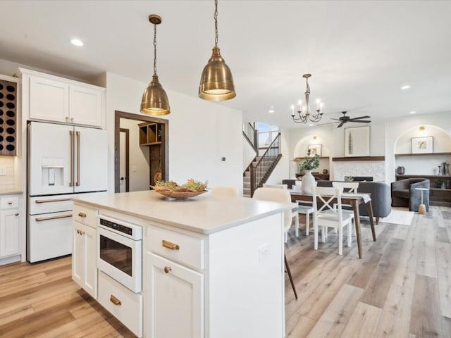 kitchen featuring white appliances, hanging light fixtures, tasteful backsplash, a kitchen island, and white cabinetry