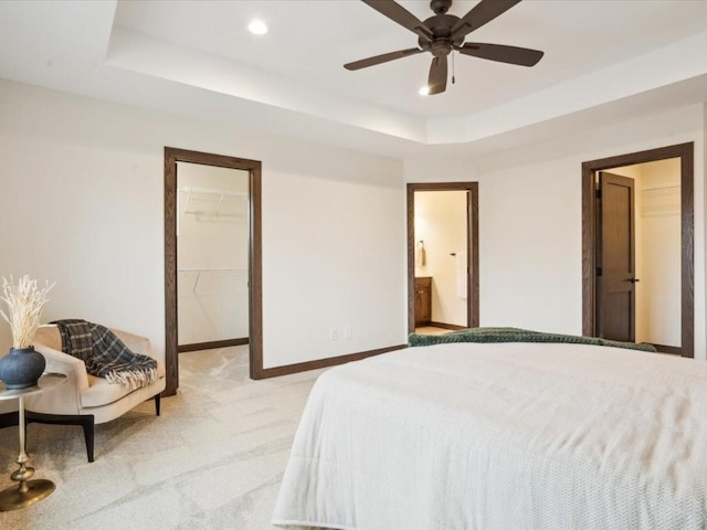 carpeted bedroom featuring a raised ceiling, a walk in closet, ceiling fan, connected bathroom, and a closet