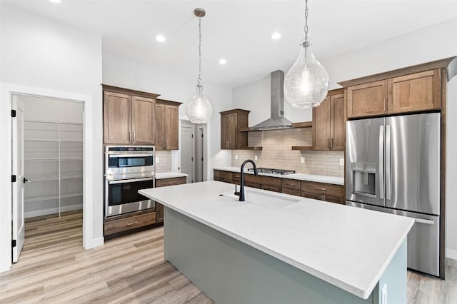 kitchen featuring sink, wall chimney exhaust hood, decorative light fixtures, a kitchen island with sink, and appliances with stainless steel finishes