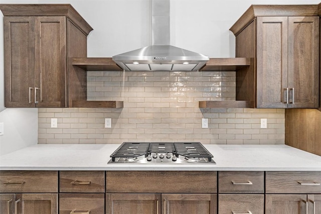 kitchen featuring tasteful backsplash, light stone counters, stainless steel gas stovetop, and wall chimney range hood