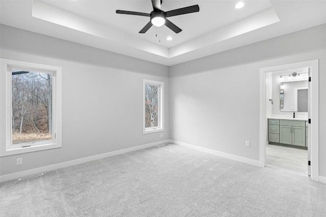 unfurnished bedroom featuring ceiling fan, a raised ceiling, light colored carpet, and ensuite bath