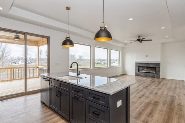 kitchen with a raised ceiling, ceiling fan, a center island with sink, and pendant lighting