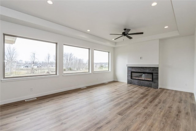 unfurnished living room with a tray ceiling, ceiling fan, a fireplace, and light wood-type flooring