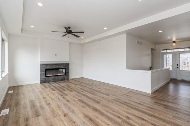 unfurnished living room with a tile fireplace, a tray ceiling, ceiling fan, and light hardwood / wood-style floors