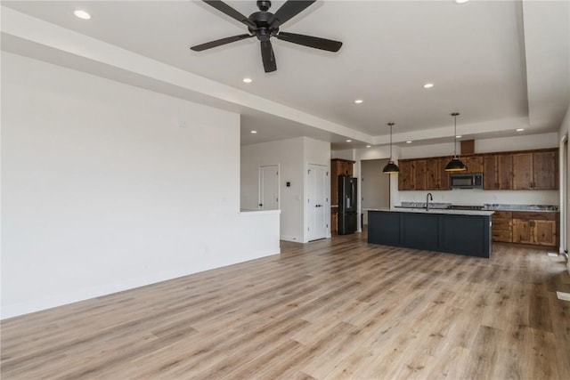 kitchen featuring black appliances, light wood-type flooring, an island with sink, a tray ceiling, and decorative light fixtures