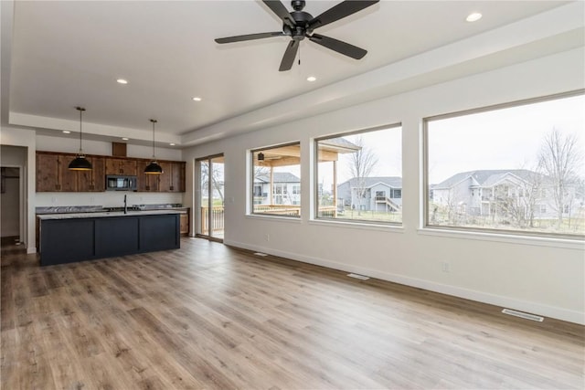 unfurnished living room with a tray ceiling, ceiling fan, hardwood / wood-style floors, and sink